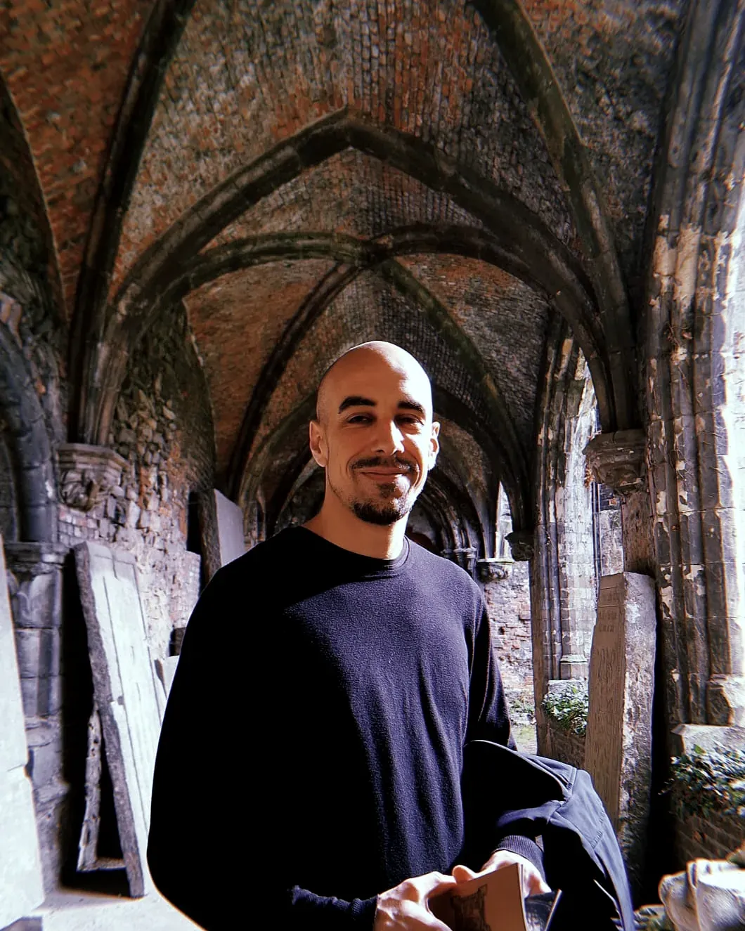 Photo of Gregory Deseck standing in a vaulted brick cloister